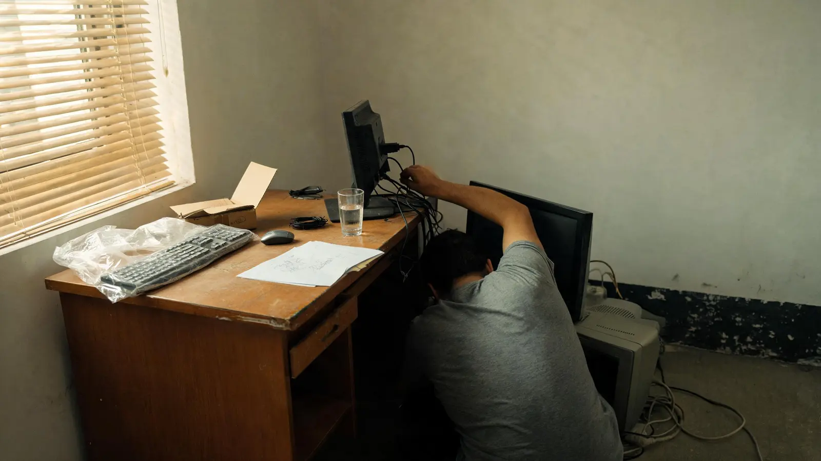 Tecnico che collega i cavi dietro il monitor di una postazione appena montata
